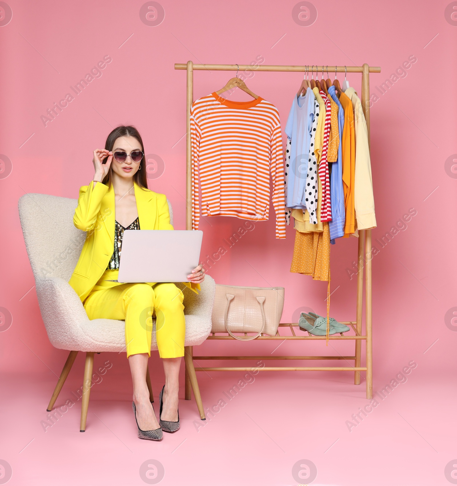 Fashion stylist with laptop and clothing rack on pink background Photo of Fashion stylist with laptop and clothing rack on pink background
