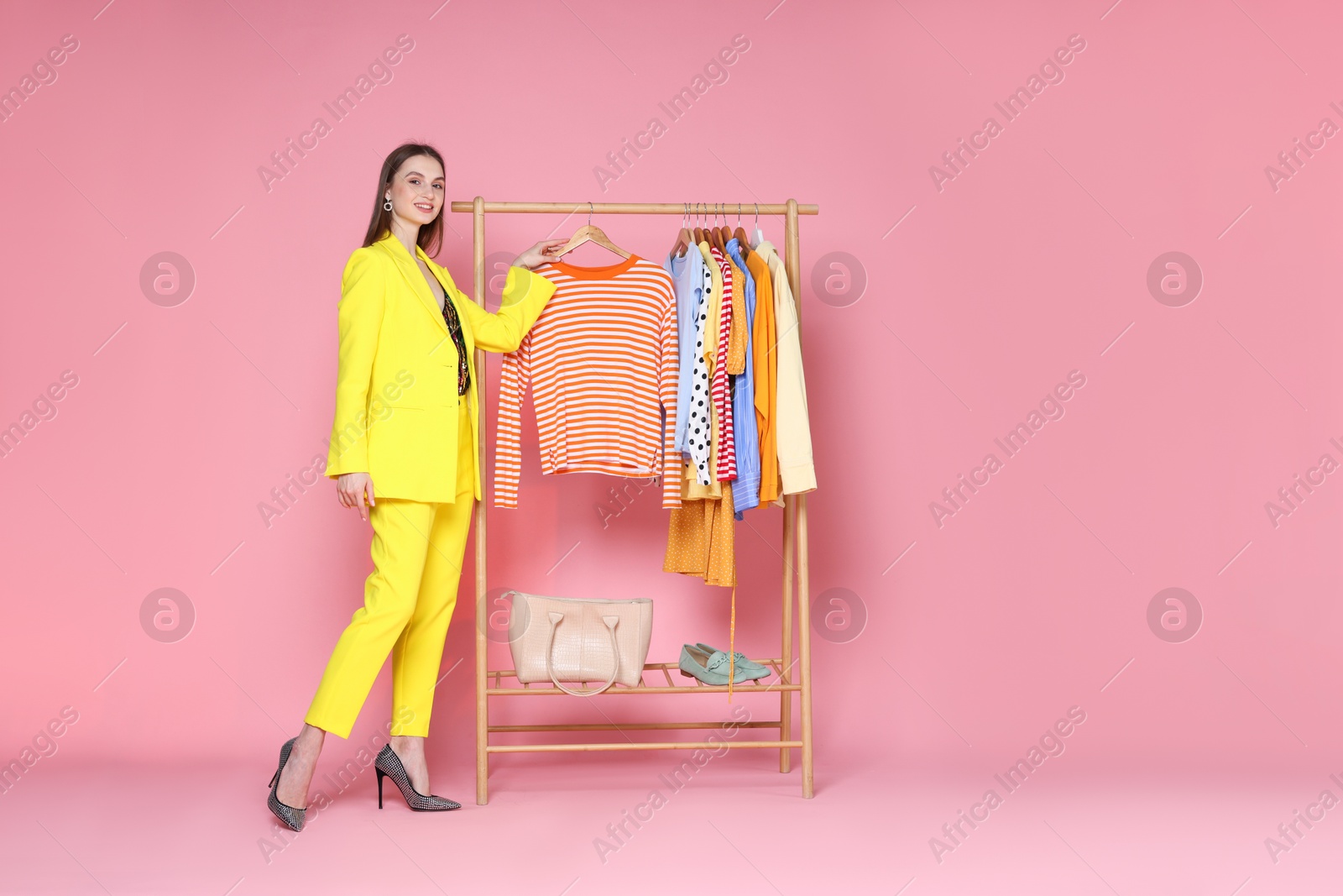Smiling fashion stylist and clothing rack on pink background. Space for text Photo of Smiling fashion stylist and clothing rack on pink background. Space for text