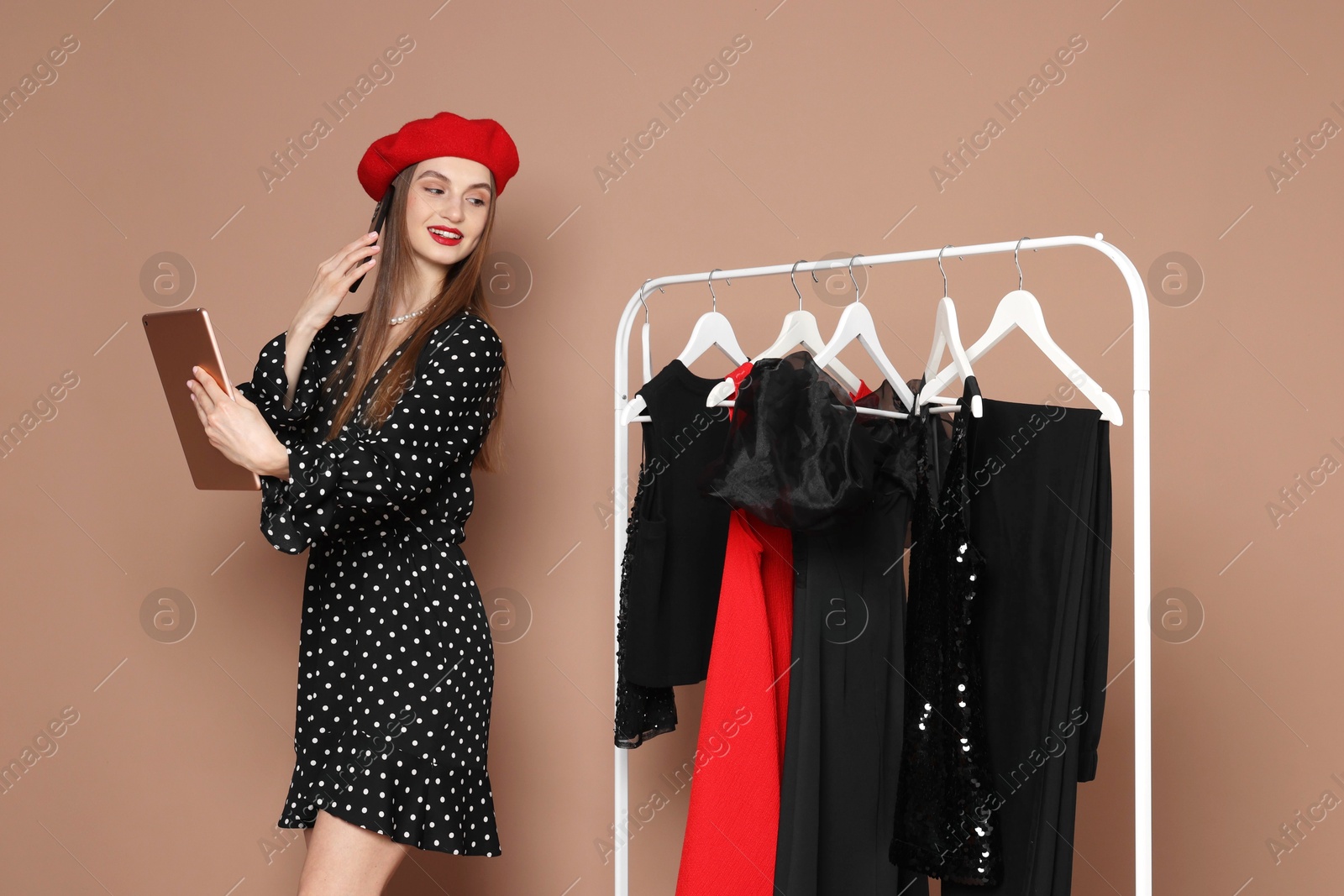 Smiling fashion stylist with tablet and clothing rack on beige background Photo of Smiling fashion stylist with tablet and clothing rack on beige background