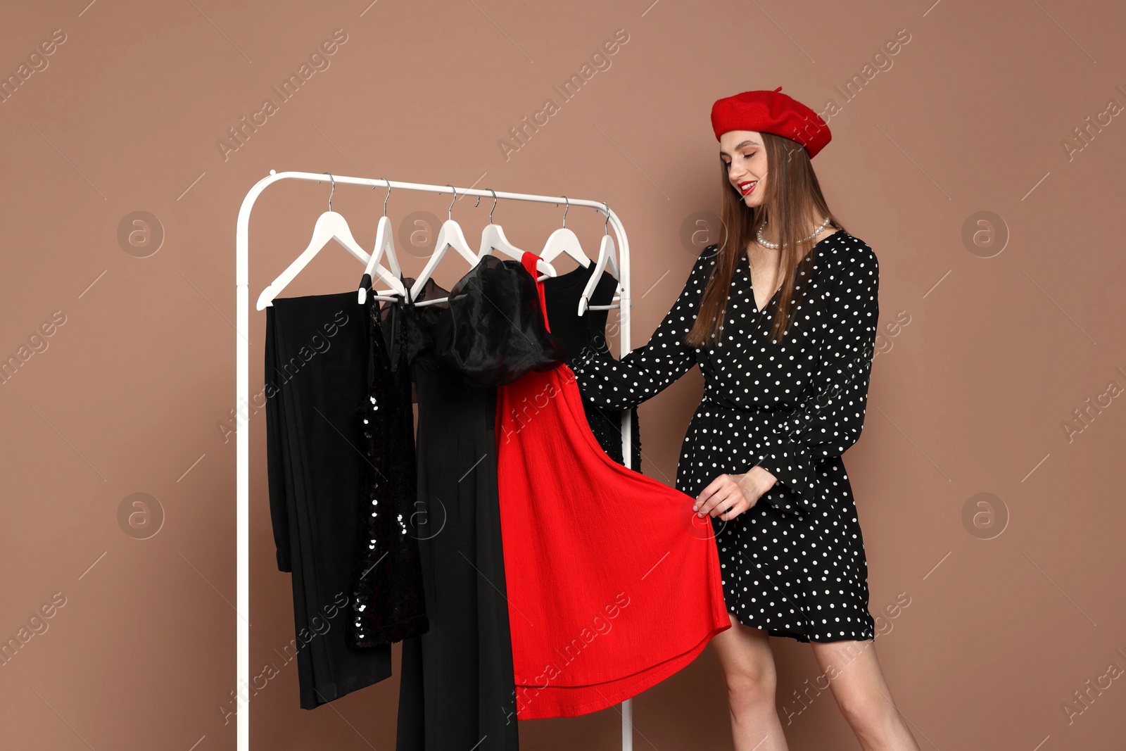 Smiling fashion stylist choosing clothes from rack on beige background Photo of Smiling fashion stylist choosing clothes from rack on beige background