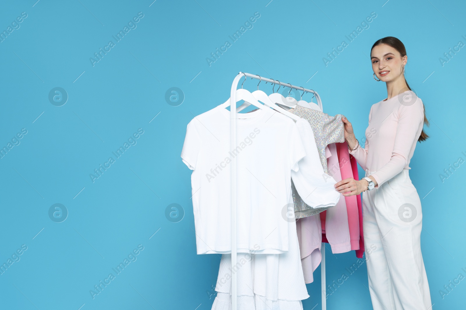 Smiling fashion stylist with clothing rack on light blue background. Space for text Photo of Smiling fashion stylist with clothing rack on light blue background. Space for text