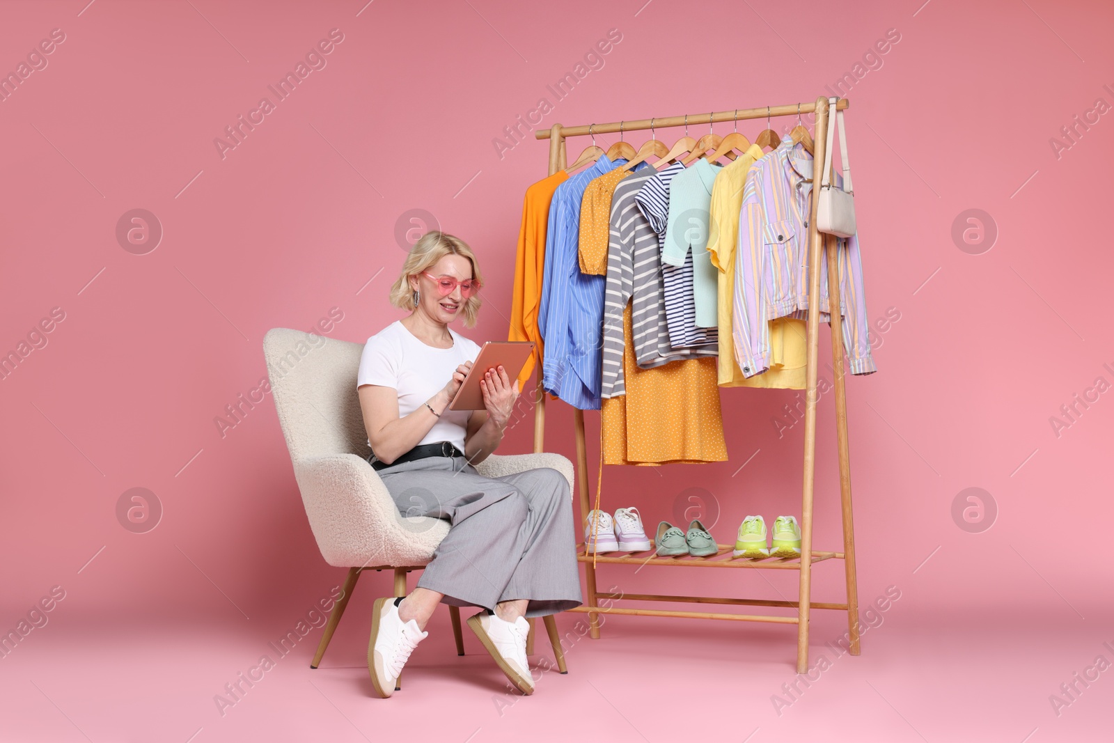 Smiling fashion stylist with tablet and clothing rack on pink background Photo of Smiling fashion stylist with tablet and clothing rack on pink background