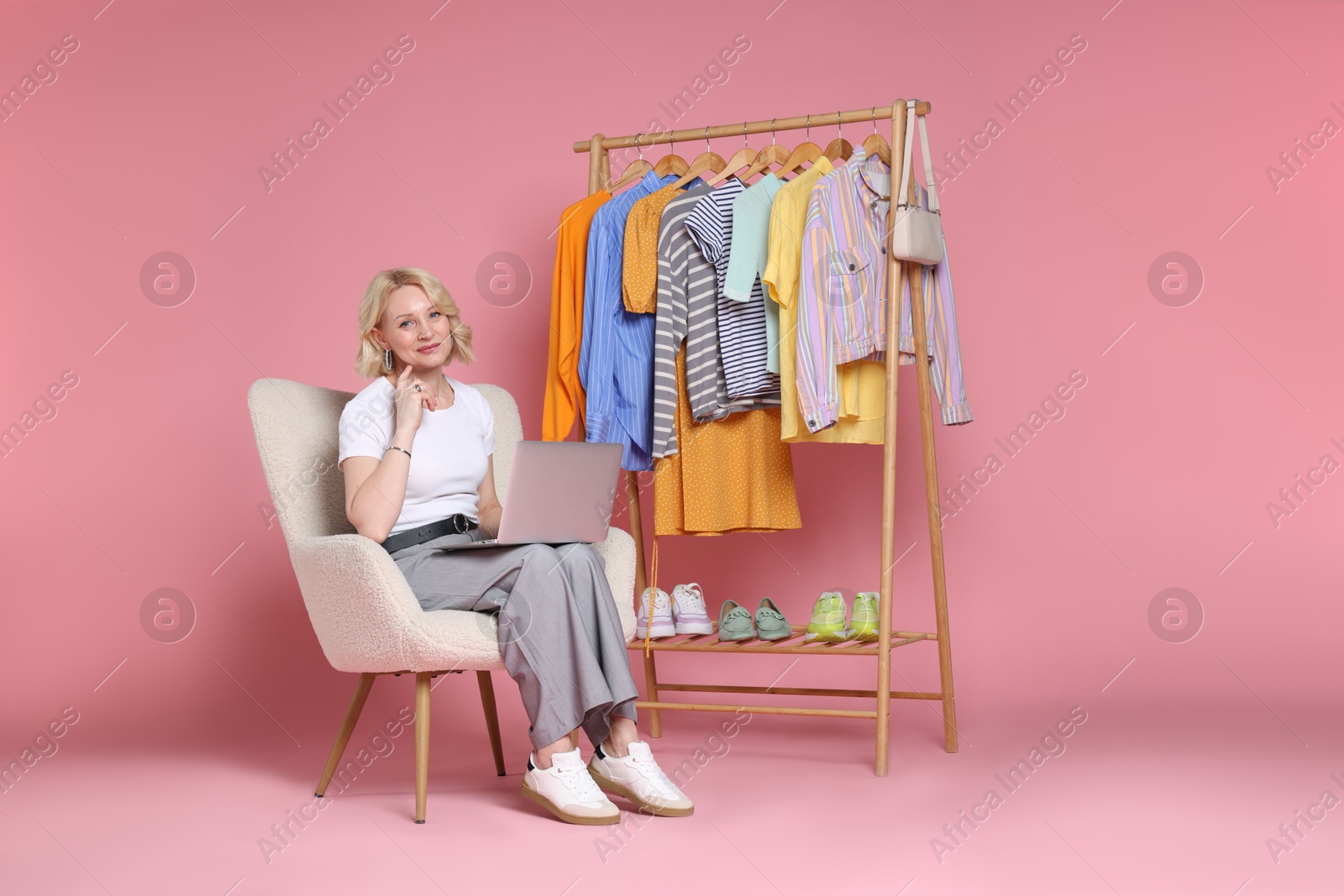 Fashion stylist with laptop and clothing rack on pink background Photo of Fashion stylist with laptop and clothing rack on pink background