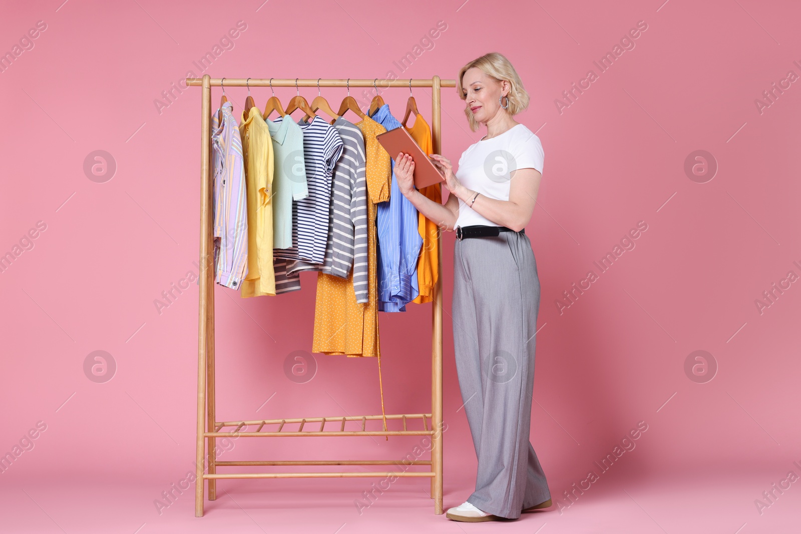 Fashion stylist with tablet and clothing rack on pink background Photo of Fashion stylist with tablet and clothing rack on pink background