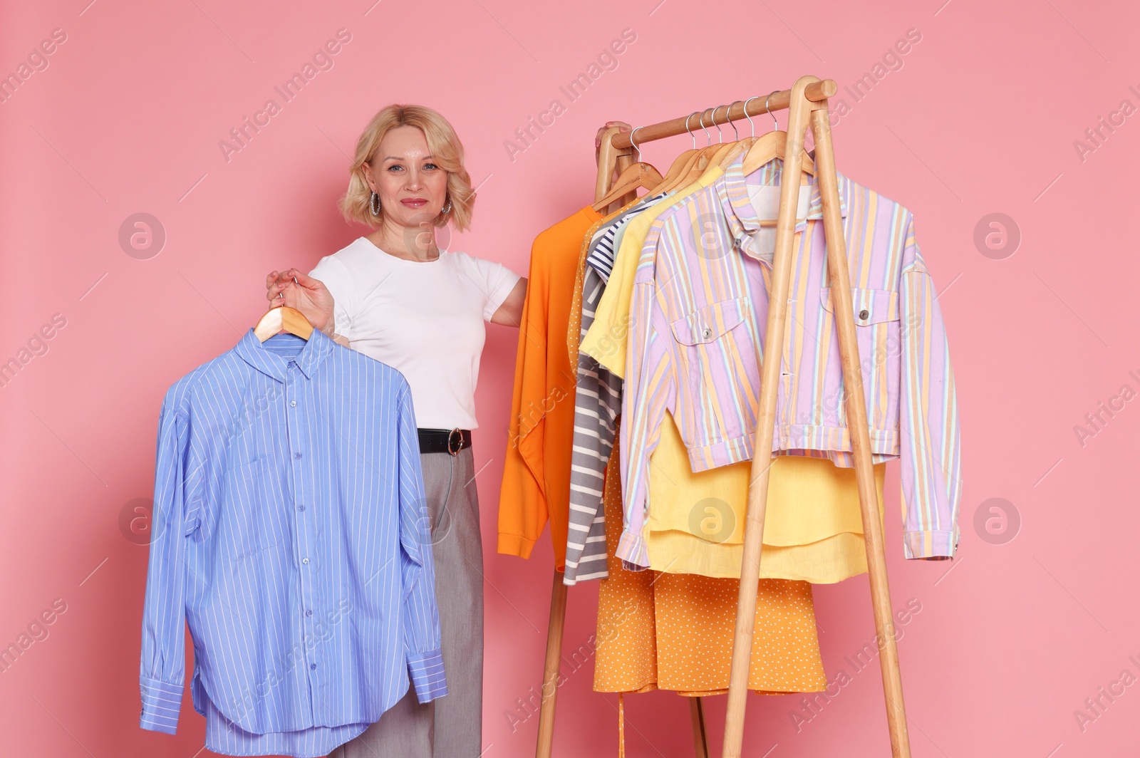 Fashion stylist and rack with clothes on pink background Photo of Fashion stylist and rack with clothes on pink background