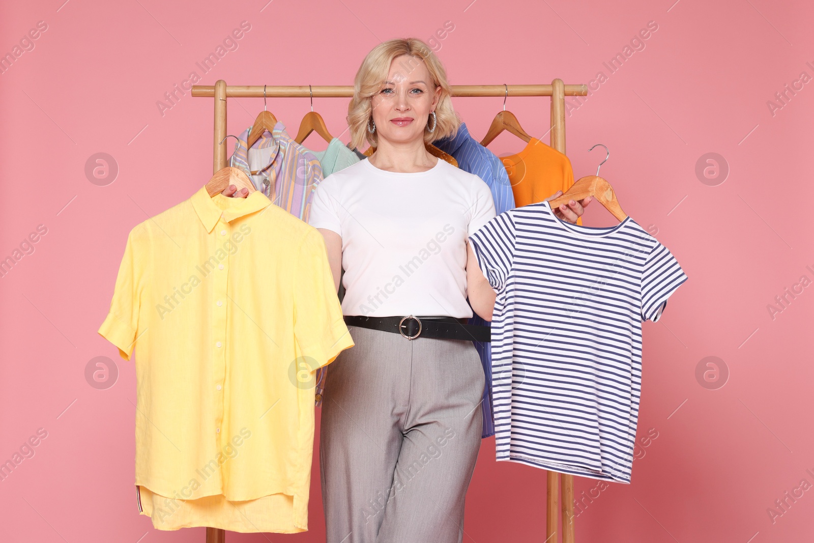 Fashion stylist and rack with clothes on pink background Photo of Fashion stylist and rack with clothes on pink background