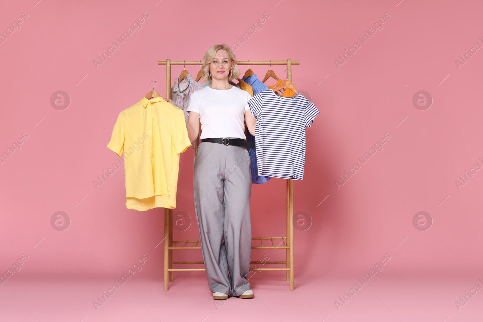 Fashion stylist and rack with clothes on pink background Photo of Fashion stylist and rack with clothes on pink background