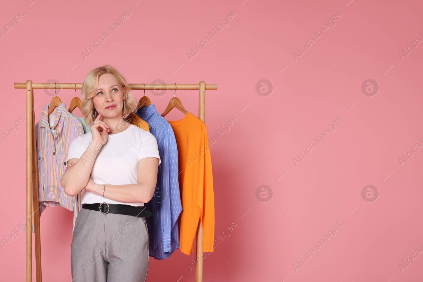 Thoughtful fashion stylist and rack with clothes on pink background. Space for text Photo of Thoughtful fashion stylist and rack with clothes on pink background. Space for text