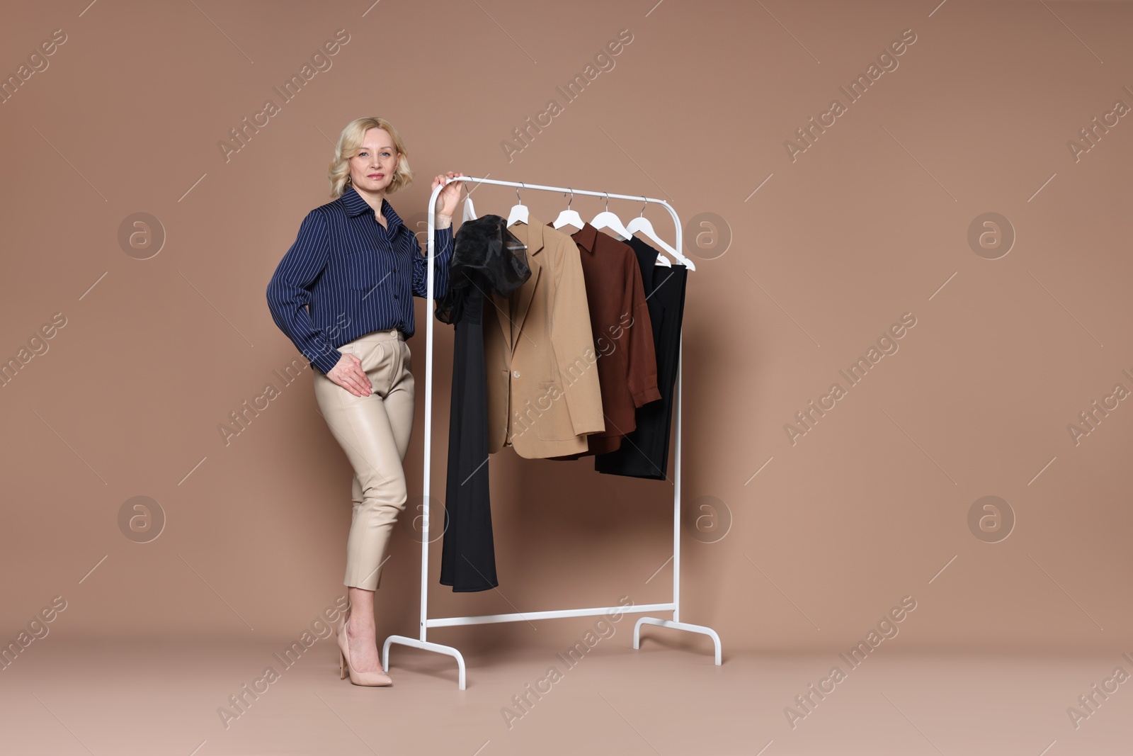 Fashion stylist and rack with clothes on beige background Photo of Fashion stylist and rack with clothes on beige background