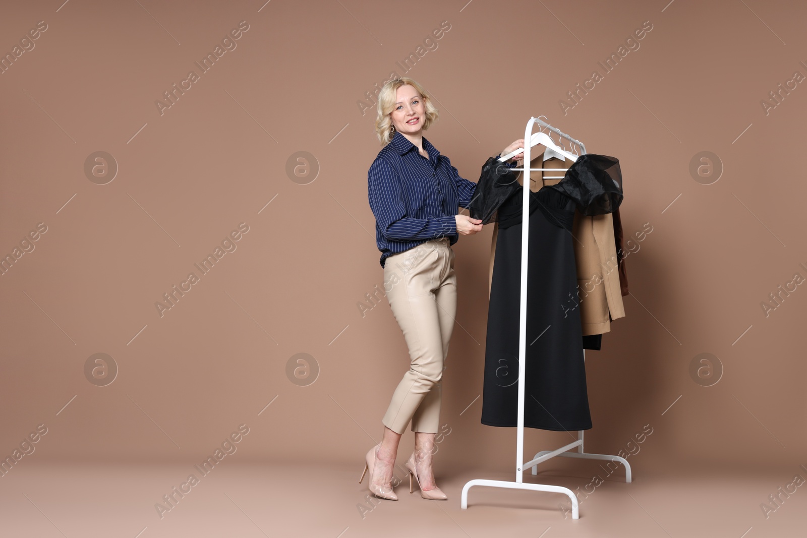 Fashion stylist and rack with clothes on beige background. Space for text Photo of Fashion stylist and rack with clothes on beige background. Space for text