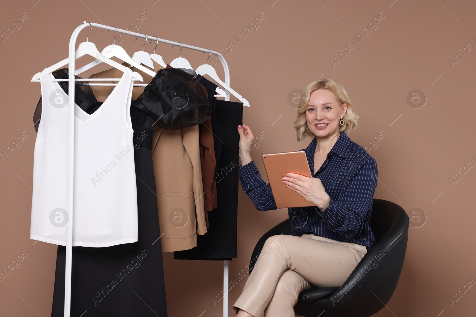 Smiling fashion stylist with tablet and clothing rack on beige background Photo of Smiling fashion stylist with tablet and clothing rack on beige background