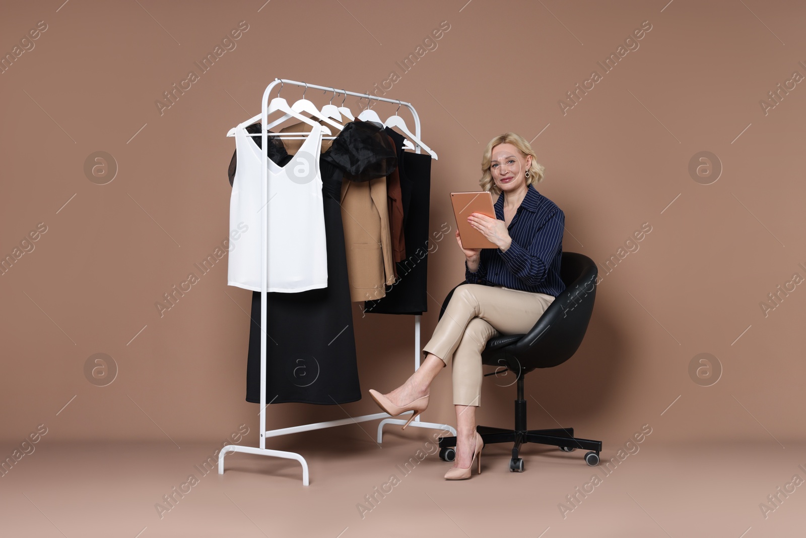 Fashion stylist with tablet and clothing rack on beige background Photo of Fashion stylist with tablet and clothing rack on beige background