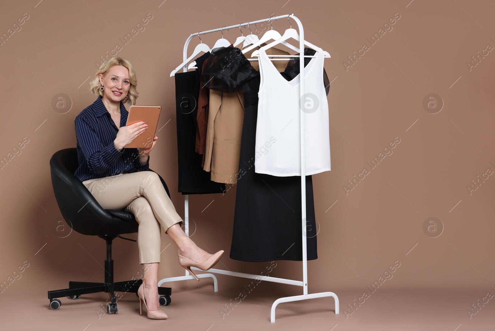 Smiling fashion stylist with tablet and clothing rack on beige background Photo of Smiling fashion stylist with tablet and clothing rack on beige background