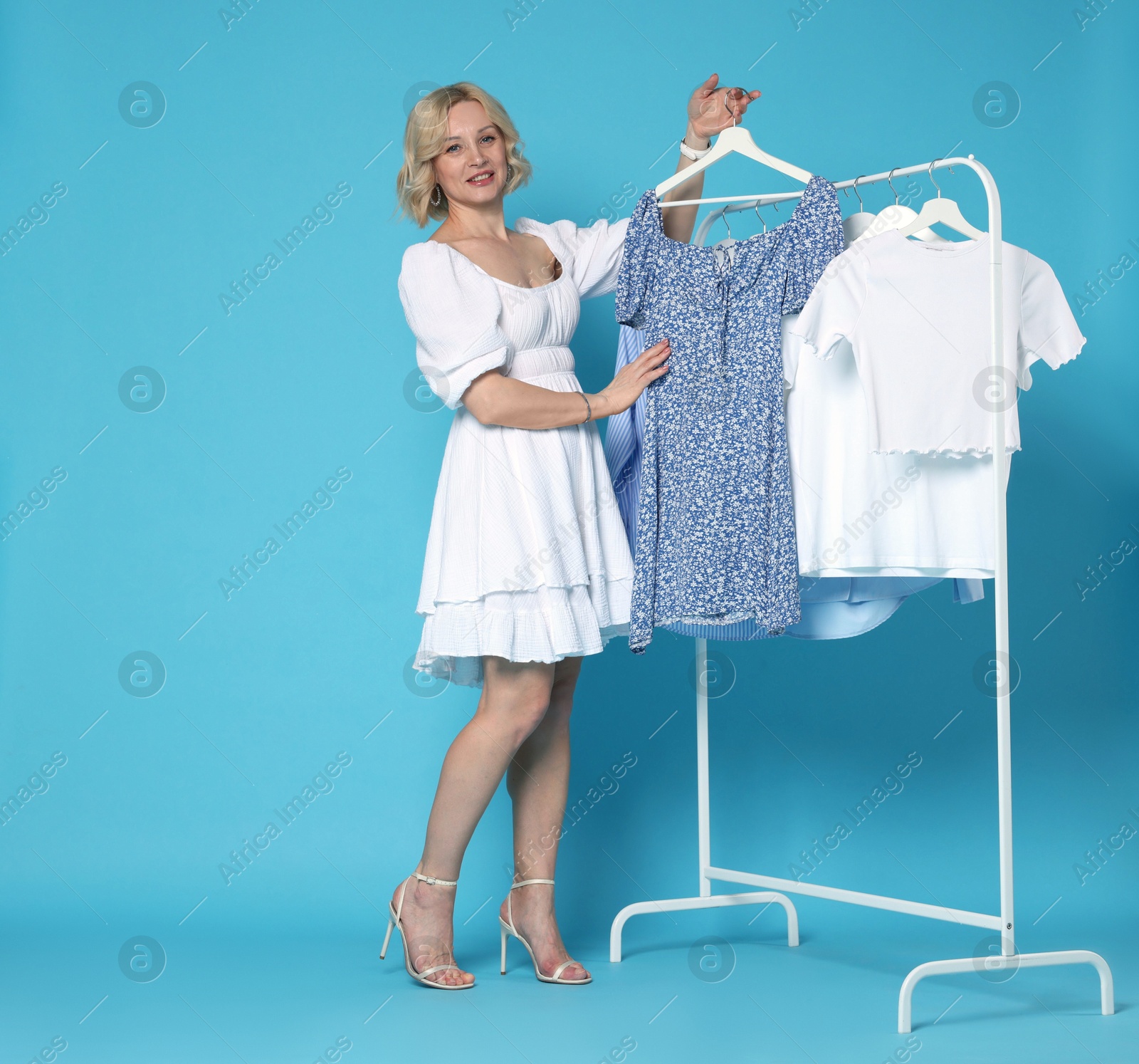 Fashion stylist and rack with clothes on light blue background Photo of Fashion stylist and rack with clothes on light blue background