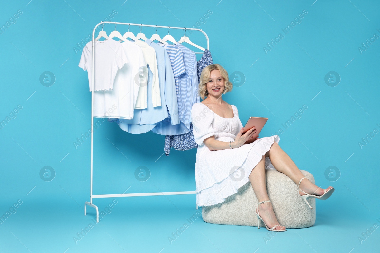 Smiling fashion stylist with tablet and clothing rack on light blue background Photo of Smiling fashion stylist with tablet and clothing rack on light blue background