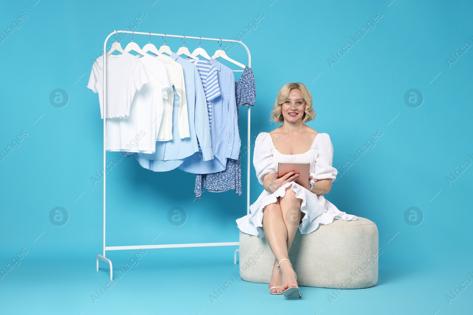 Smiling fashion stylist with tablet and clothing rack on light blue background Photo of Smiling fashion stylist with tablet and clothing rack on light blue background