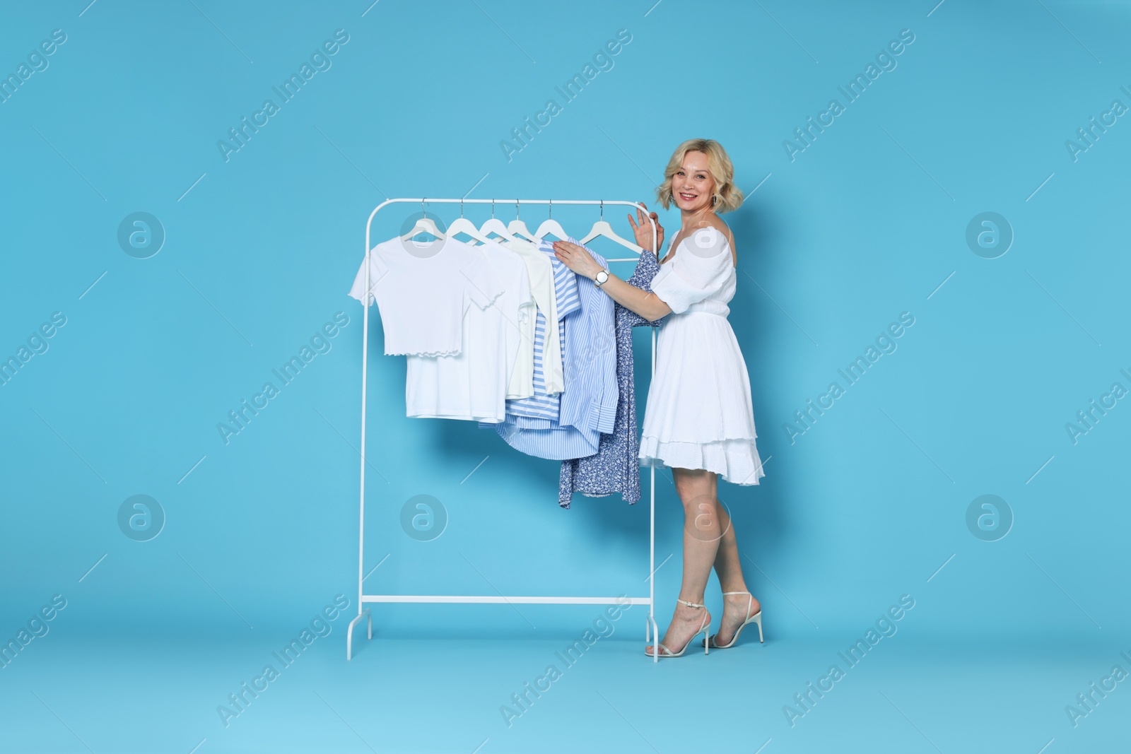 Smiling fashion stylist and rack with clothes on light blue background Photo of Smiling fashion stylist and rack with clothes on light blue background
