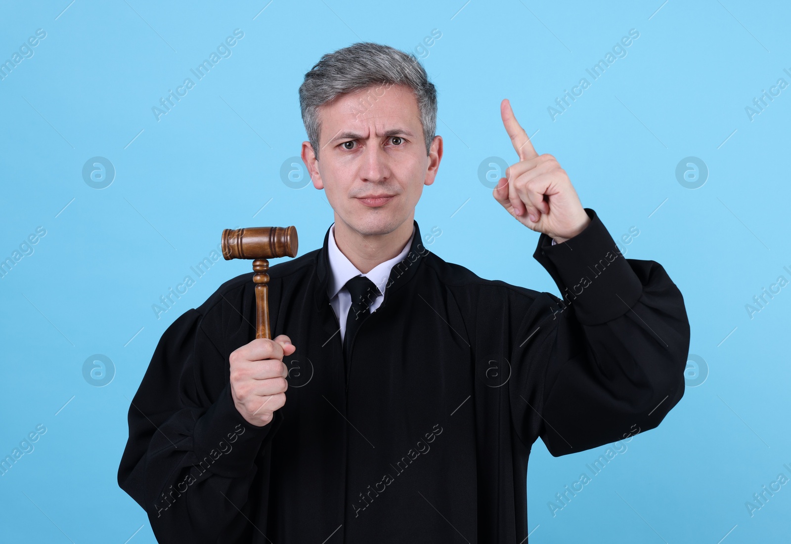 Emotional judge with mallet on light blue background Photo of Emotional judge with mallet on light blue background