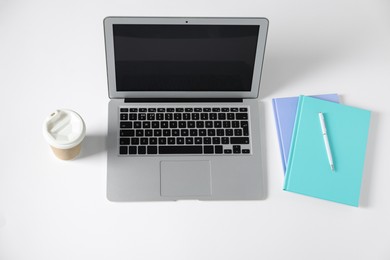 Photo of Office supplies, laptop and takeaway paper cup on white table, above view