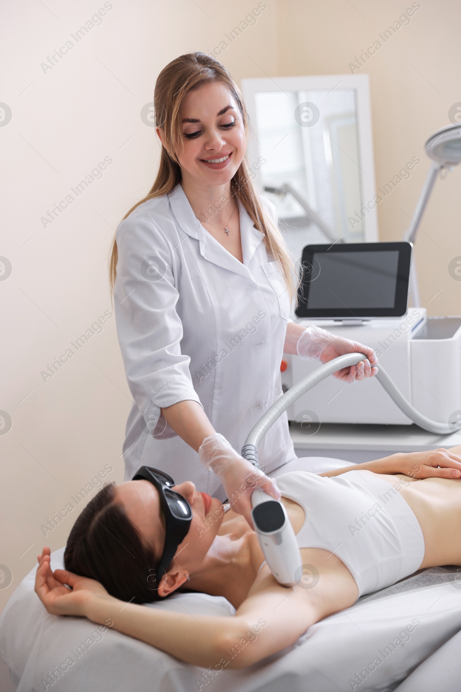 Laser hair removal procedure. Smiling cosmetologist working with client in beauty salon Photo of Laser hair removal procedure. Smiling cosmetologist working with client in beauty salon