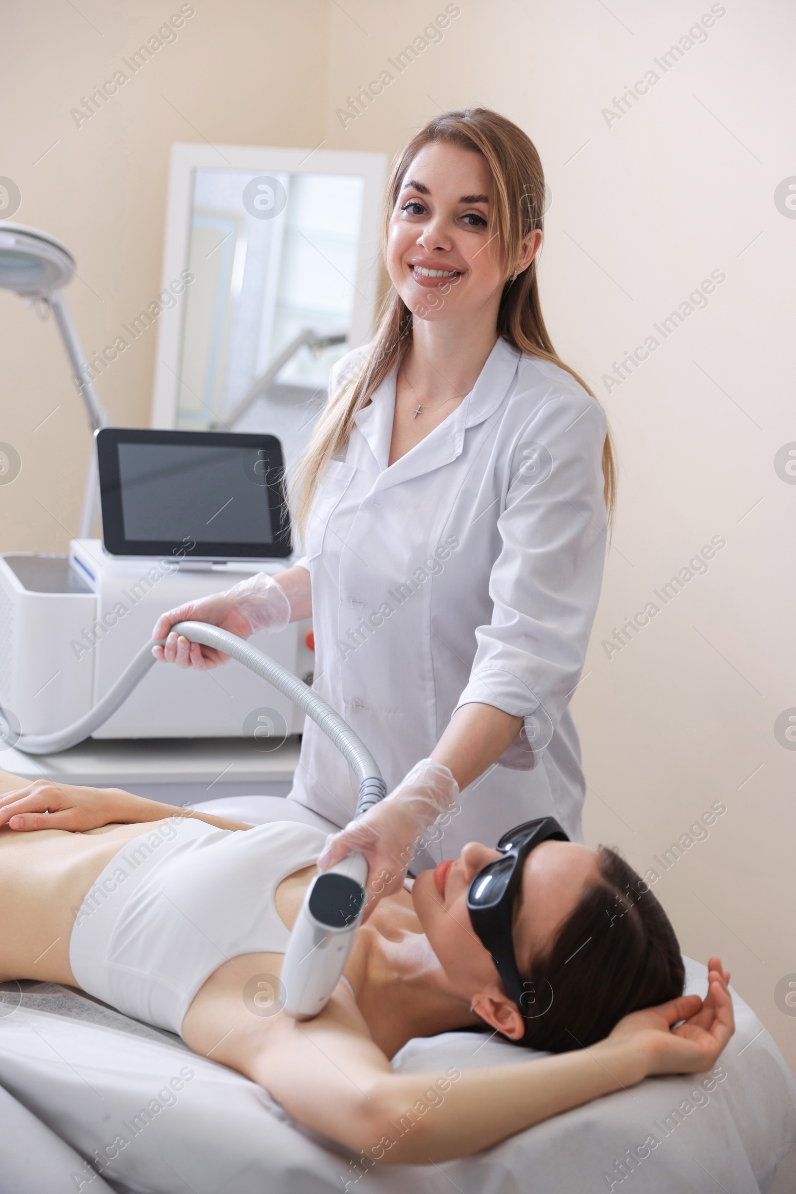 Laser hair removal procedure. Smiling cosmetologist working with client in beauty salon Photo of Laser hair removal procedure. Smiling cosmetologist working with client in beauty salon