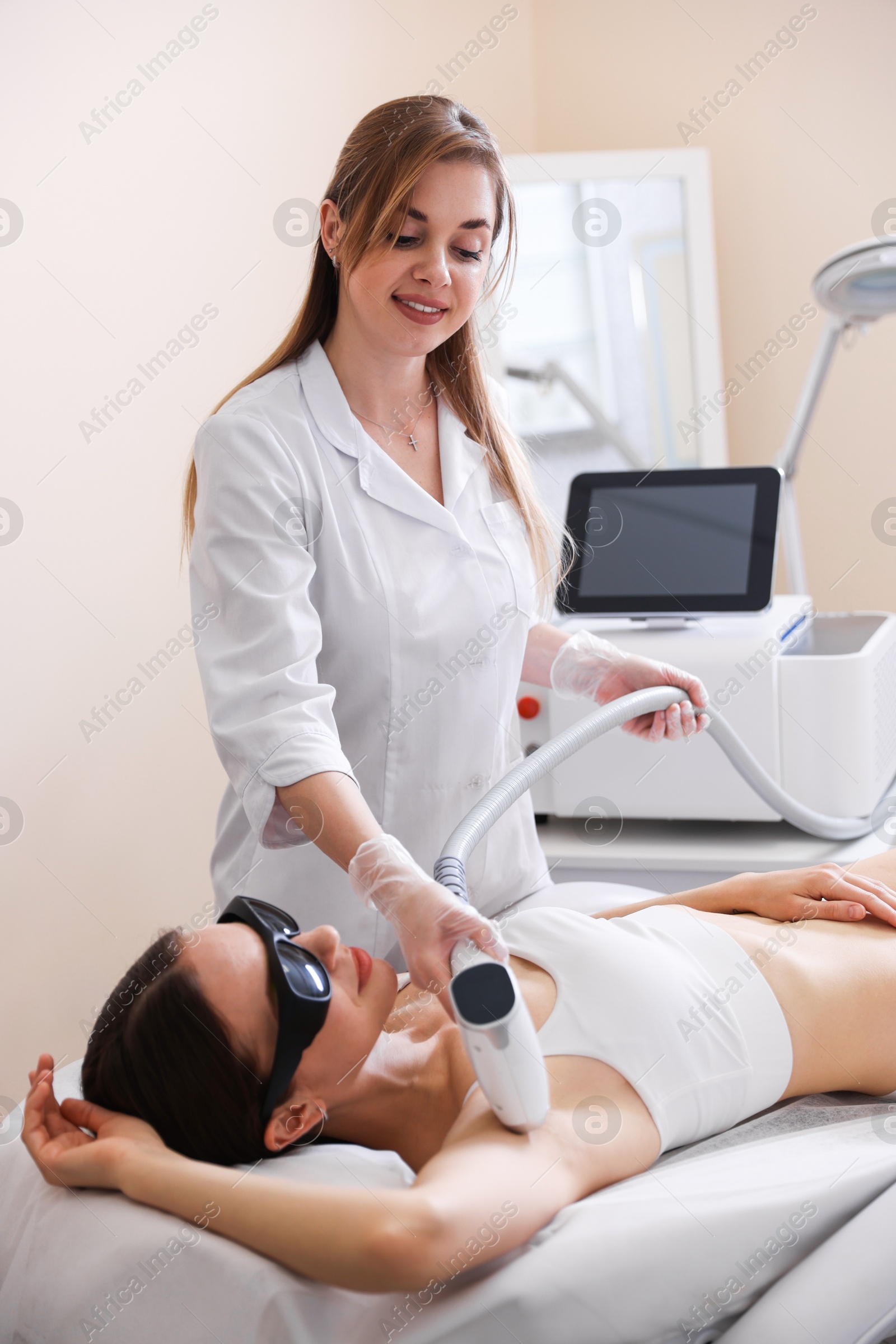 Laser hair removal procedure. Smiling cosmetologist working with client in beauty salon Photo of Laser hair removal procedure. Smiling cosmetologist working with client in beauty salon