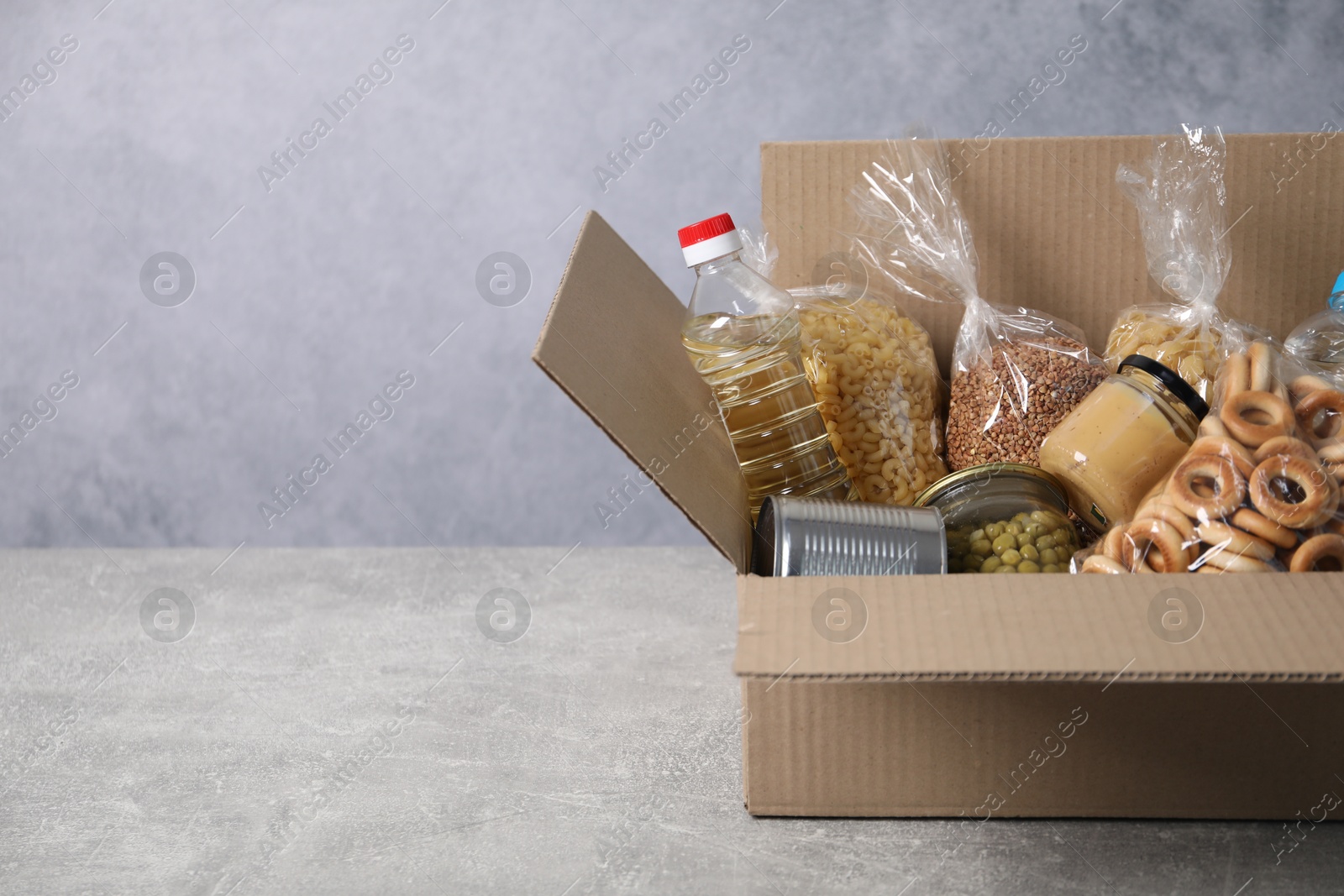 Different food products in box on gray textured table, space for text Photo of Different food products in box on gray textured table, space for text