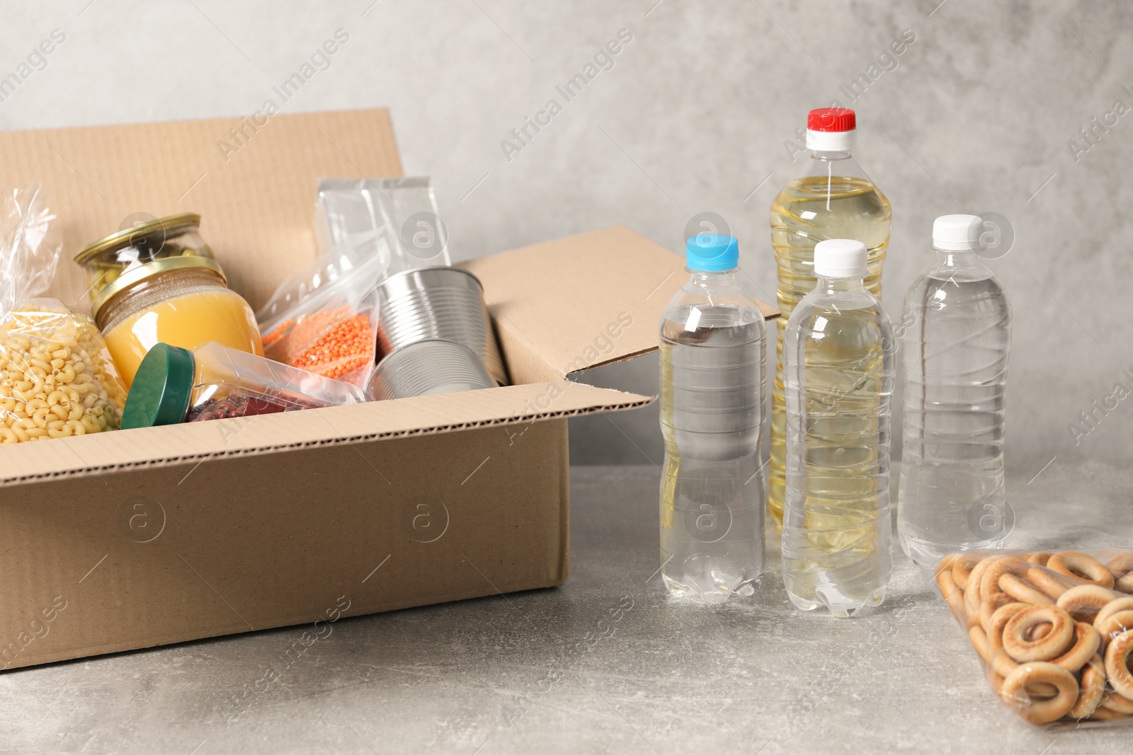 Bottles of water and different food products in box on gray textured table Photo of Bottles of water and different food products in box on gray textured table