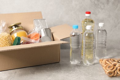 Photo of Bottles of water and different food products in box on gray textured table