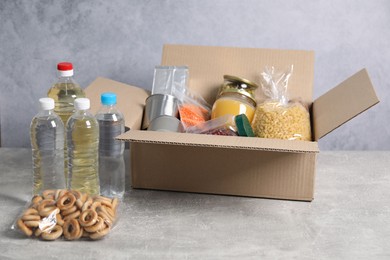 Photo of Bottles of water and different food products in box on gray textured table
