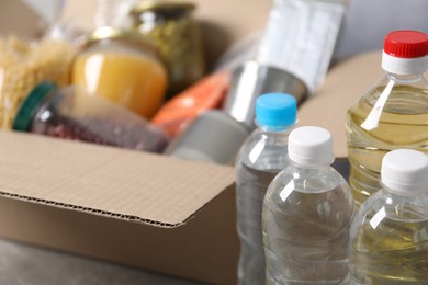 Photo of Bottles of water and different food products in box on table, closeup
