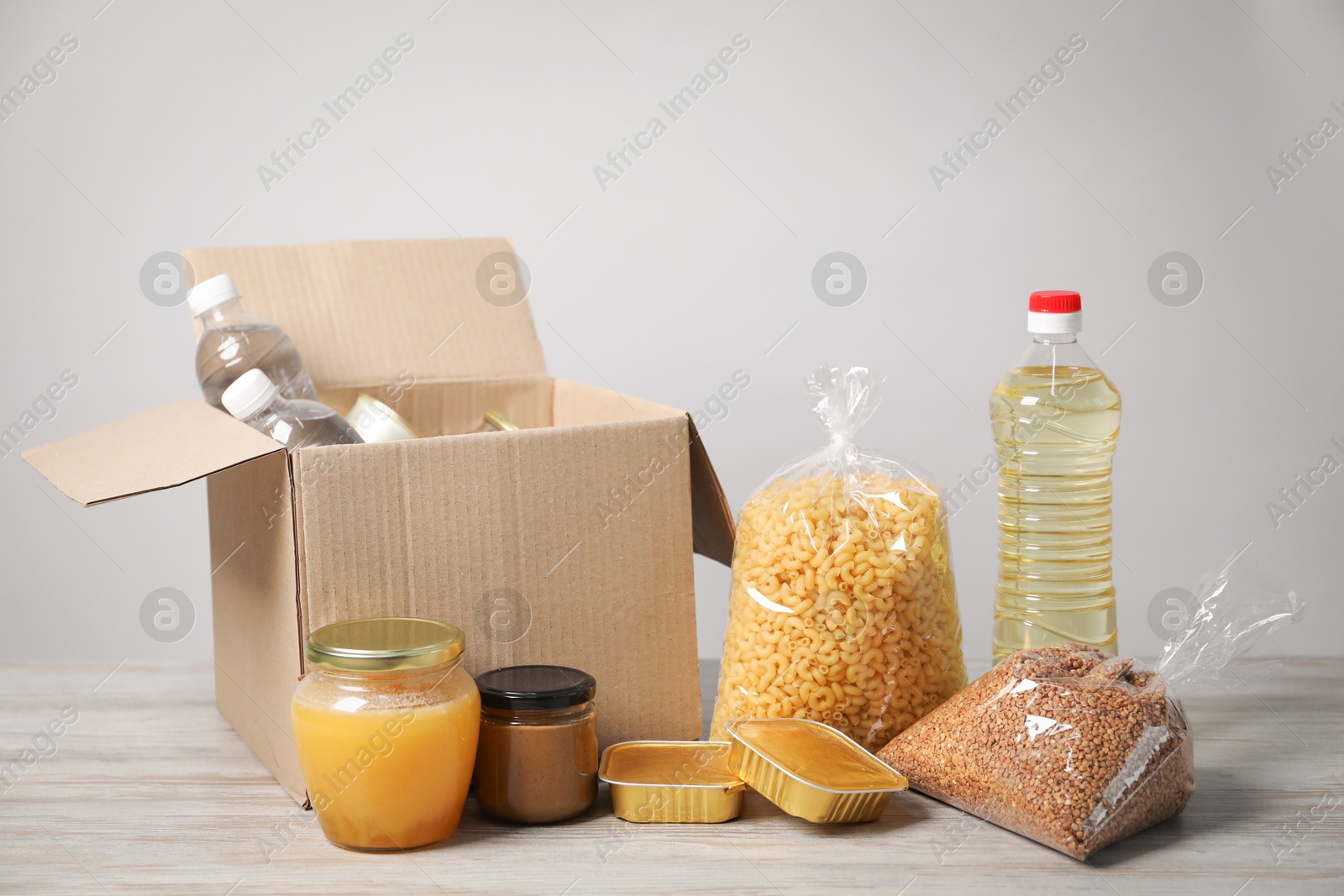 Different food products and box on wooden table against light background Photo of Different food products and box on wooden table against light background