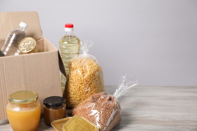 Photo of Different food products and box on wooden table against light background, space for text