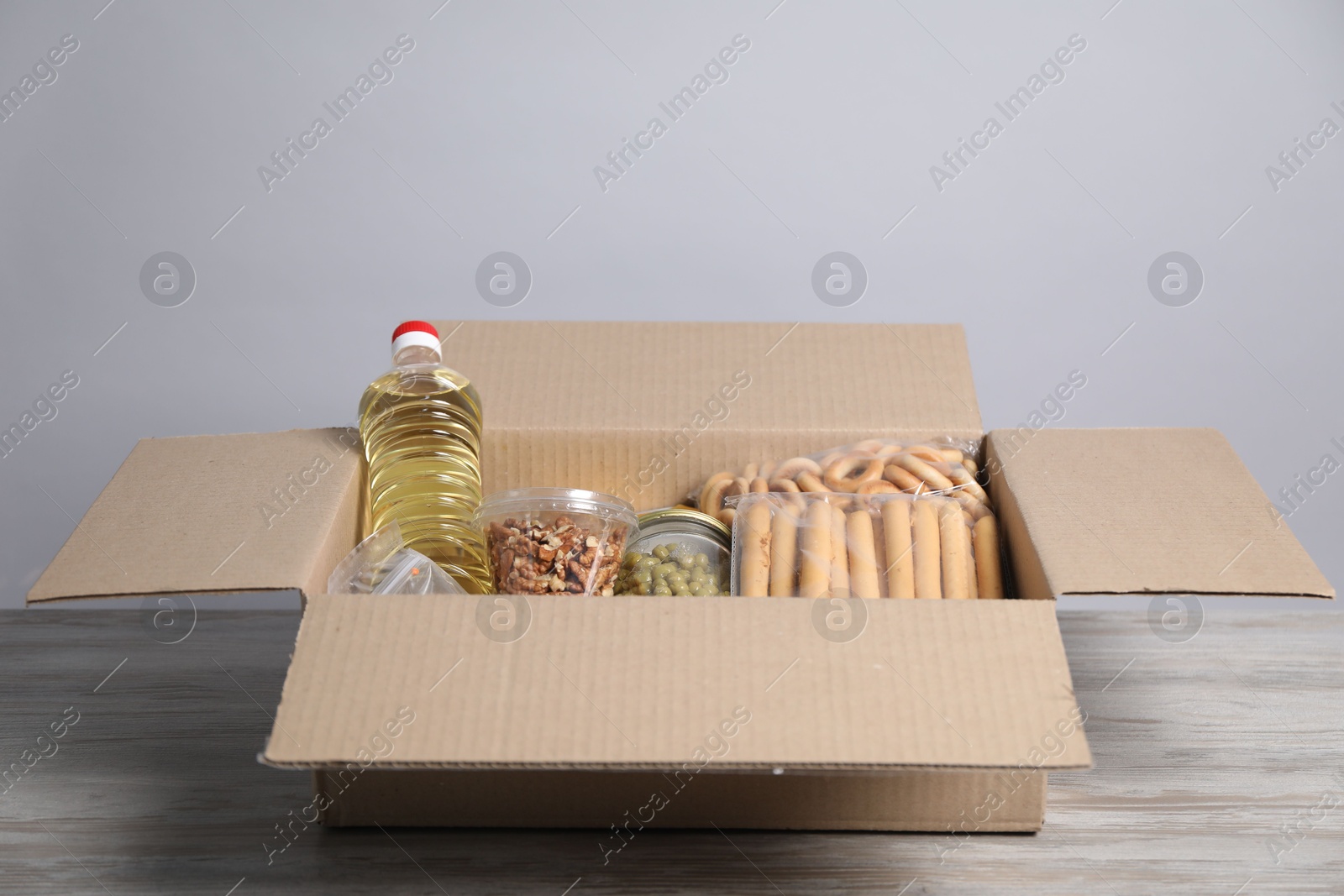 Different food products in box on wooden table against light background Photo of Different food products in box on wooden table against light background