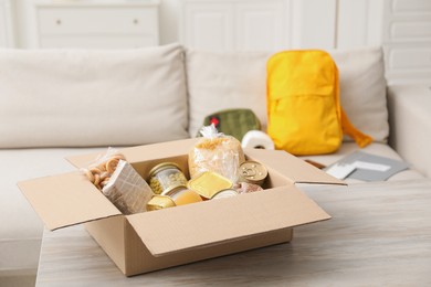 Photo of Survival kit. Different emergency supplies and food products in box on wooden table indoors, selective focus