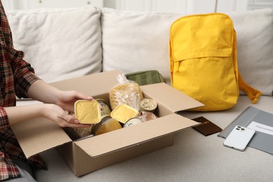 Photo of Survival kit. Woman packing different emergency supplies on sofa indoors, closeup