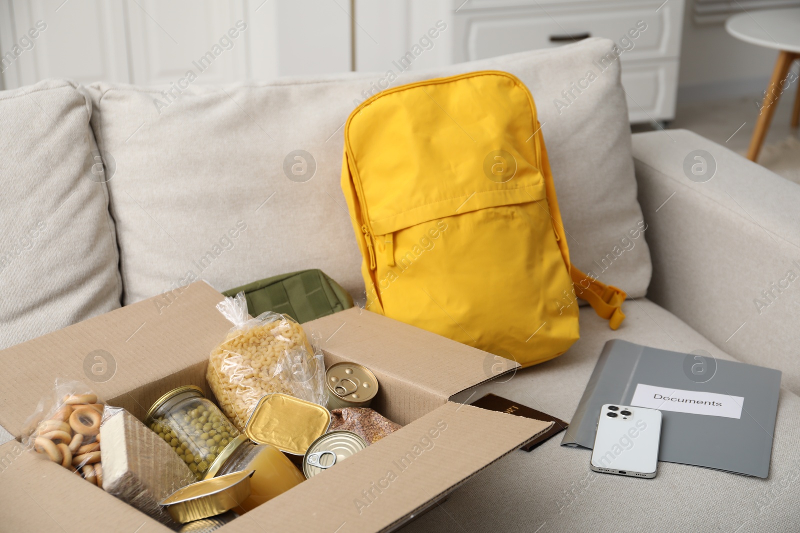 Survival kit. Different emergency supplies and food products in box on sofa Photo of Survival kit. Different emergency supplies and food products in box on sofa