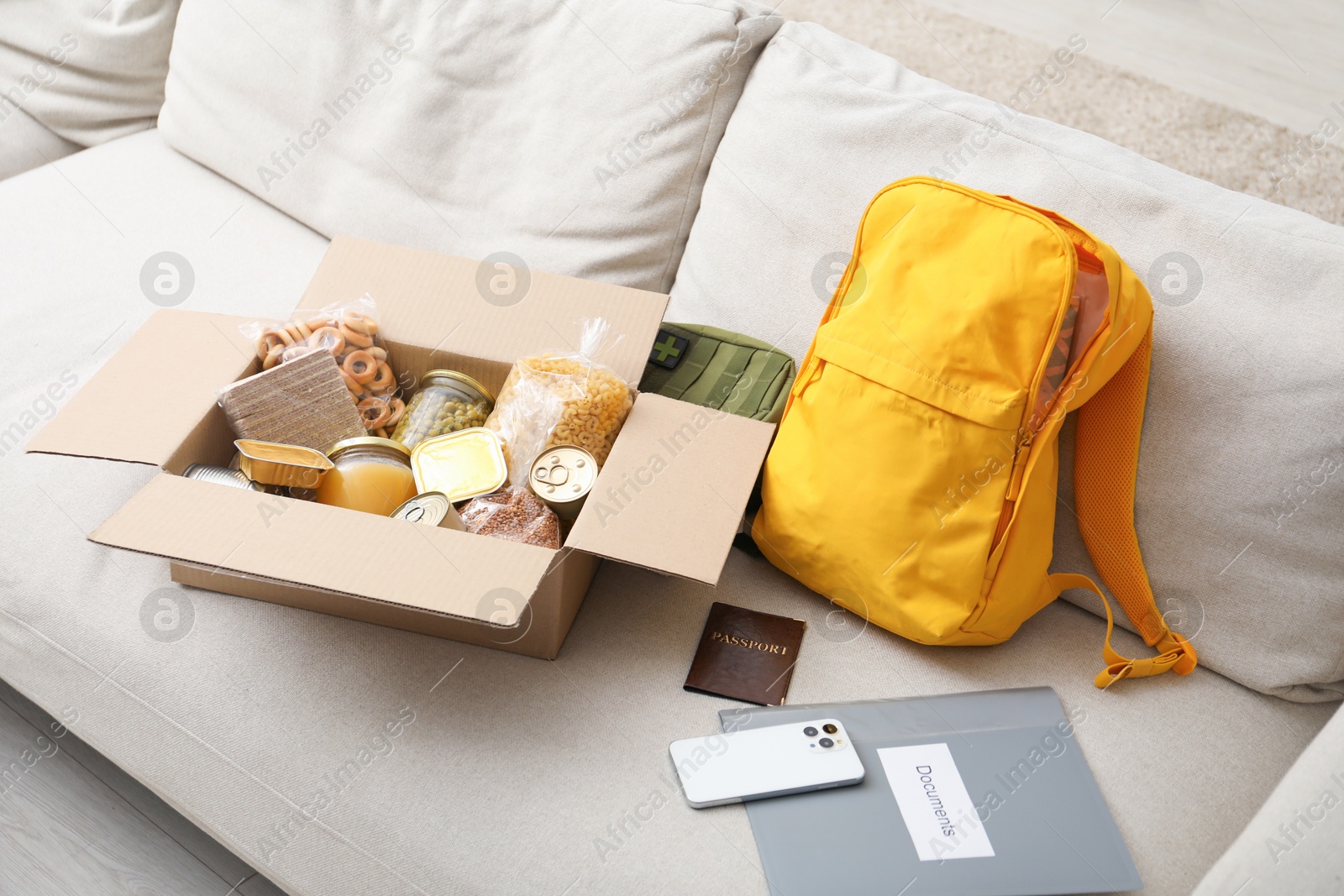 Survival kit. Different emergency supplies and food products in box on sofa Photo of Survival kit. Different emergency supplies and food products in box on sofa