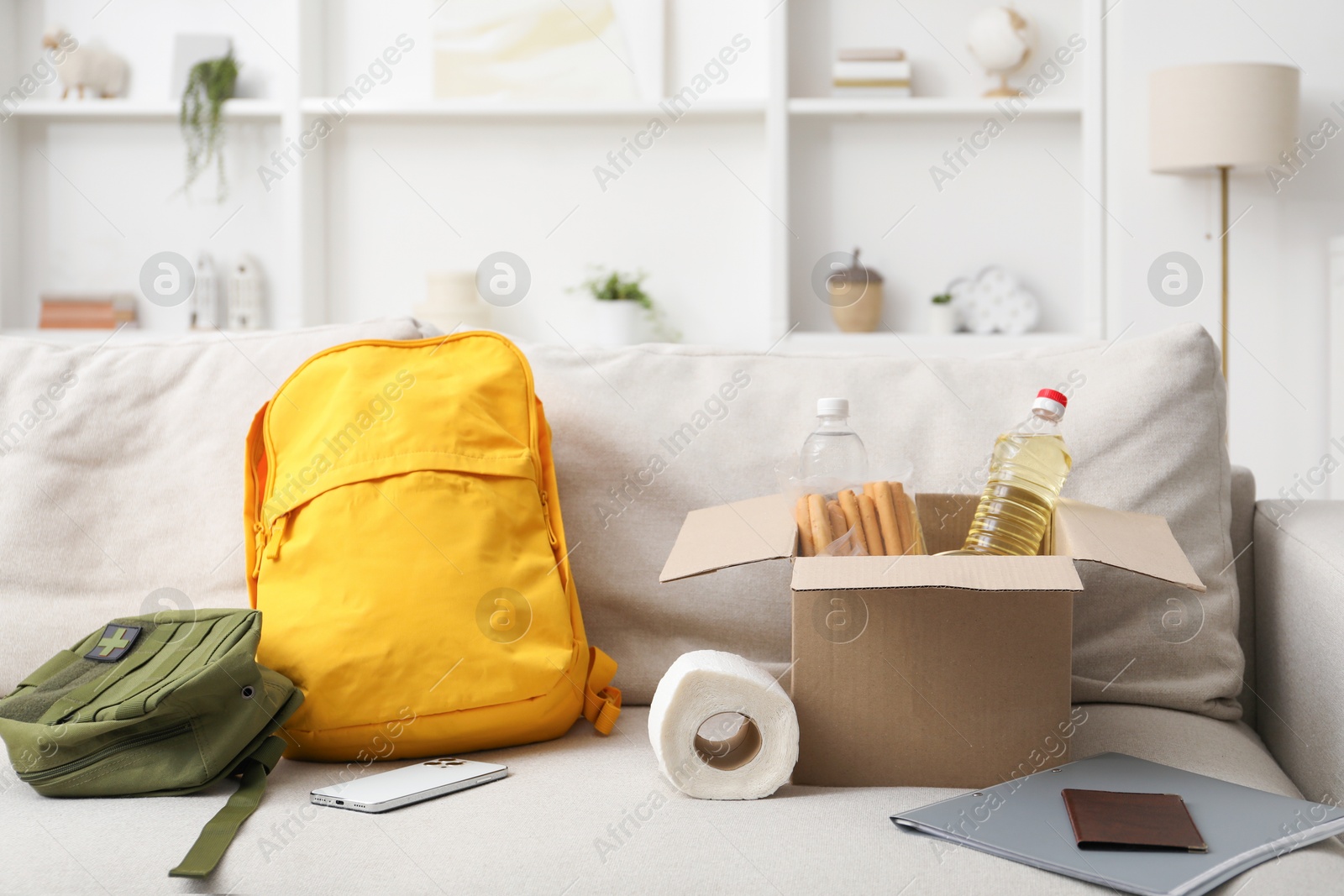 Survival kit. Different emergency supplies and food products in box on sofa Photo of Survival kit. Different emergency supplies and food products in box on sofa