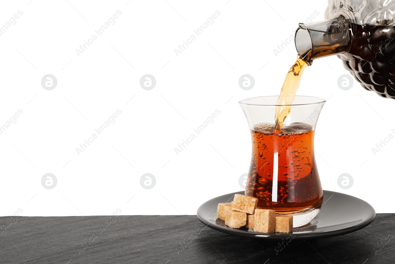 Pouring hot Turkish tea into glass cup at table against white background, closeup Photo of Pouring hot Turkish tea into glass cup at table against white background, closeup
