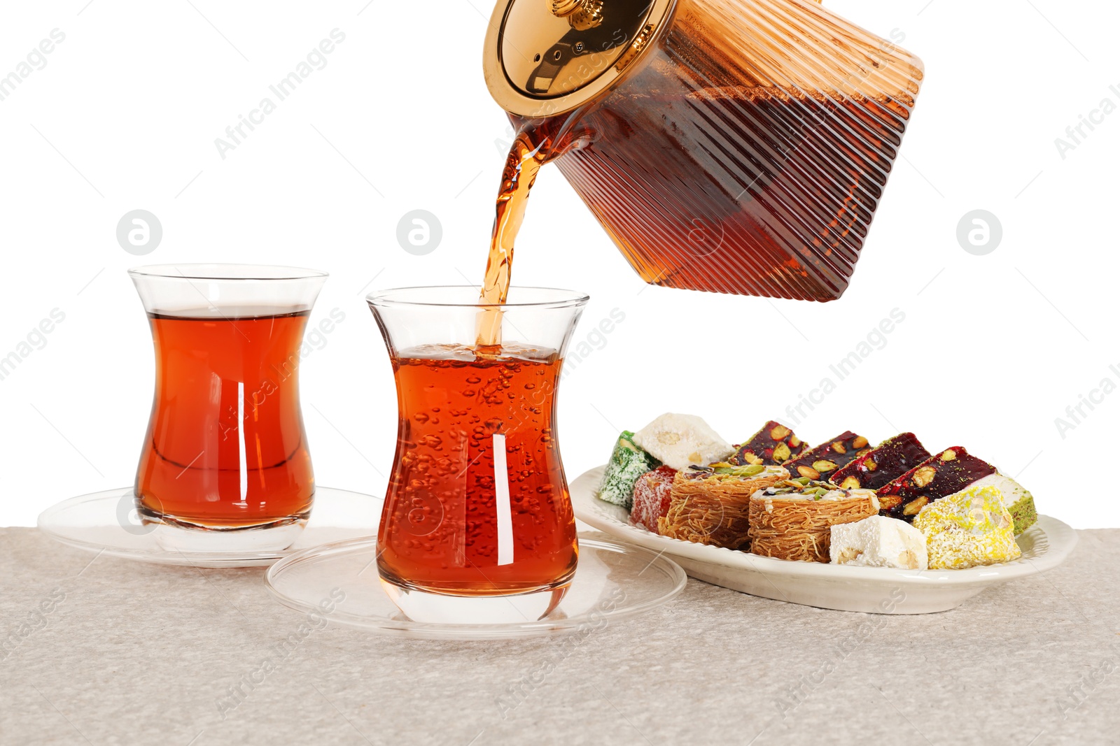 Pouring hot Turkish tea into glass cup at table against white background, closeup Photo of Pouring hot Turkish tea into glass cup at table against white background, closeup