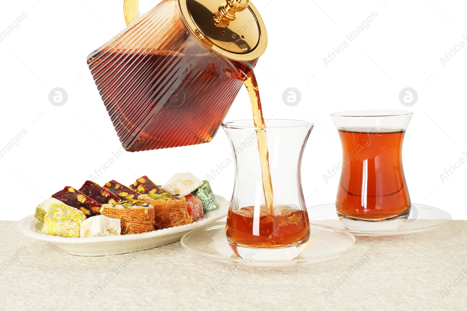 Pouring hot Turkish tea into glass cup at table against white background, closeup Photo of Pouring hot Turkish tea into glass cup at table against white background, closeup