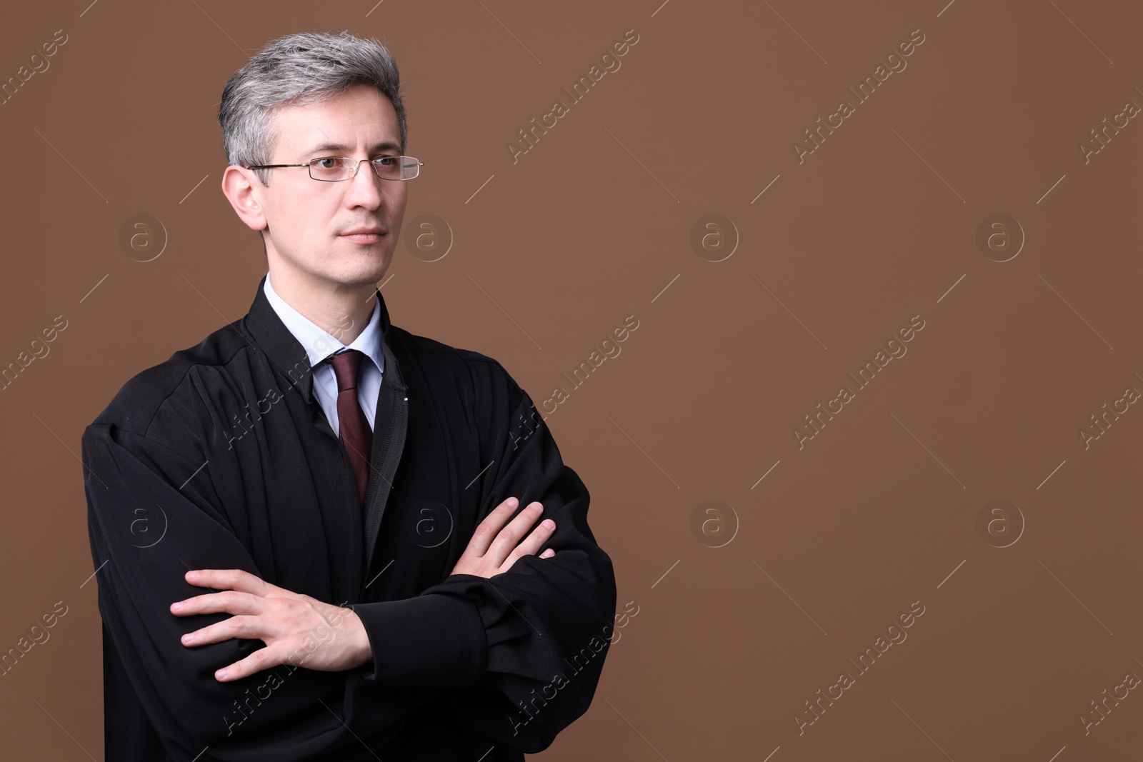 Judge in court dress with crossed arms on brown background. Space for text Photo of Judge in court dress with crossed arms on brown background. Space for text