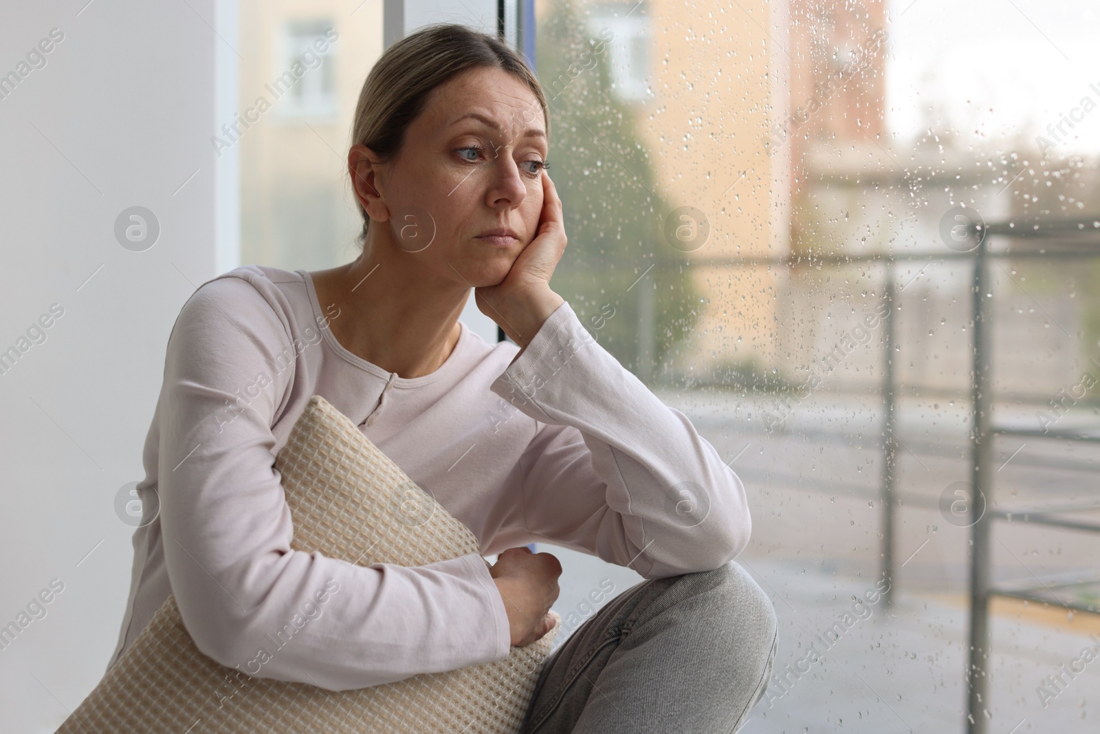 Depressed woman looking out window at home, space for text Photo of Depressed woman looking out window at home, space for text