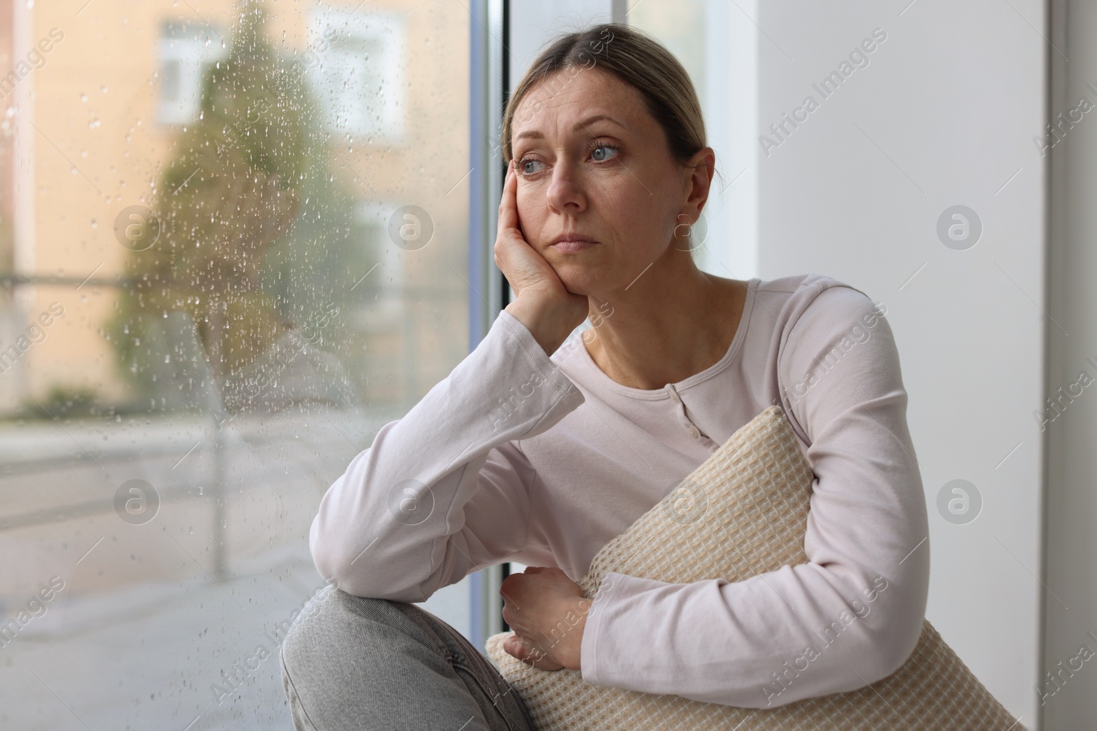 Depressed woman looking out window at home, space for text Photo of Depressed woman looking out window at home, space for text