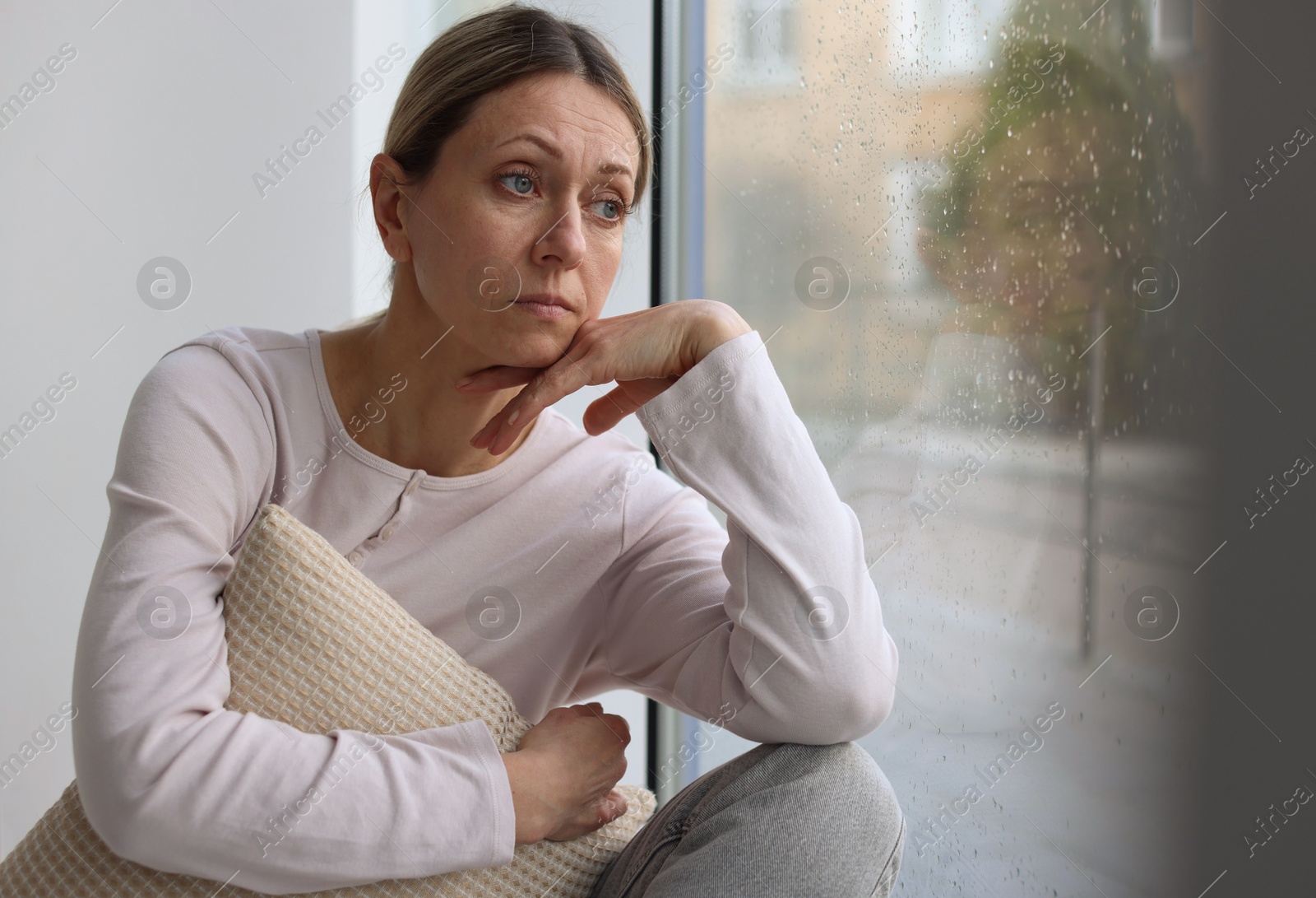Depressed woman looking out window at home, space for text Photo of Depressed woman looking out window at home, space for text