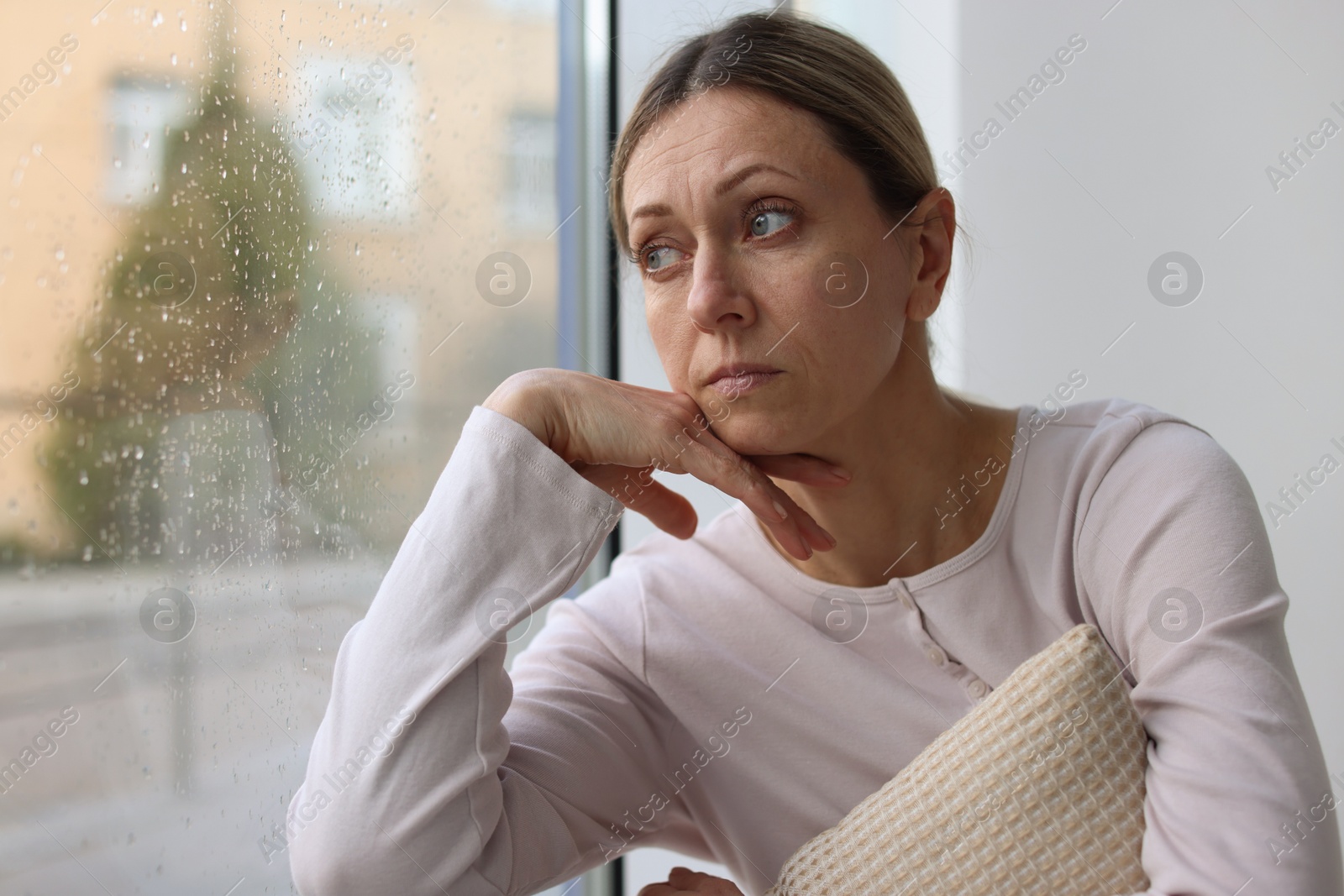 Depressed woman looking out window at home, space for text Photo of Depressed woman looking out window at home, space for text
