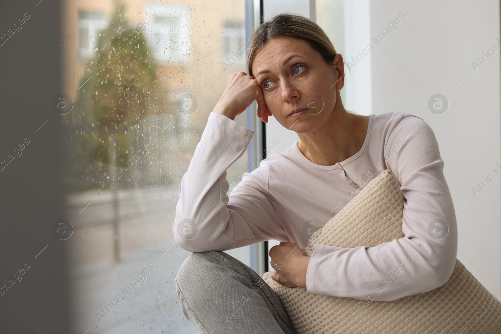 Depressed woman looking out window at home, space for text Photo of Depressed woman looking out window at home, space for text