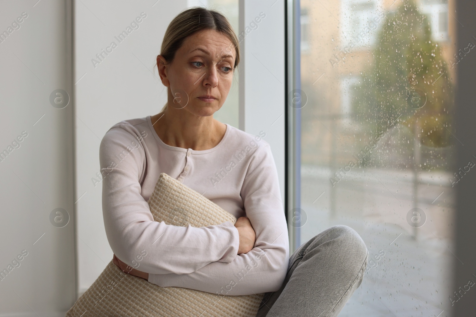 Depressed woman looking out window at home, space for text Photo of Depressed woman looking out window at home, space for text