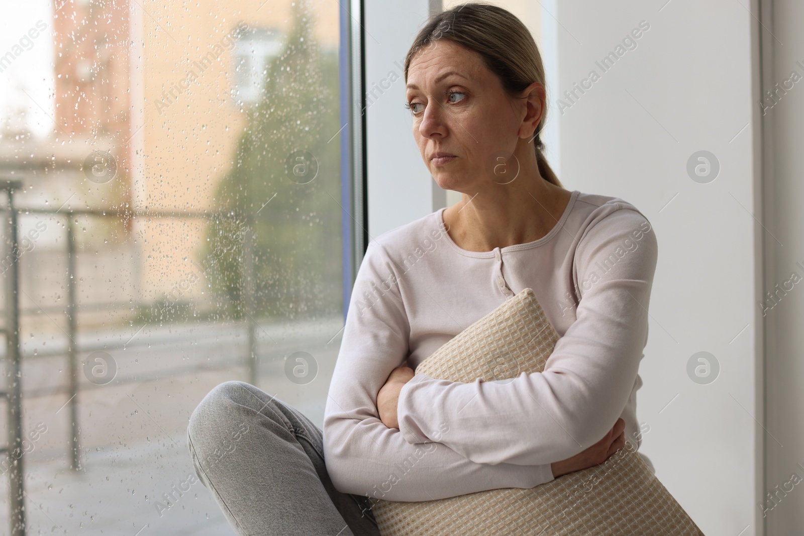 Depressed woman looking out window at home, space for text Photo of Depressed woman looking out window at home, space for text